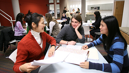 Three females students work together over a table full of papers in study hall