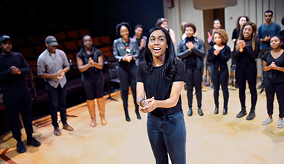 Students perform warmup exercises by clapping hands with team leader in center 