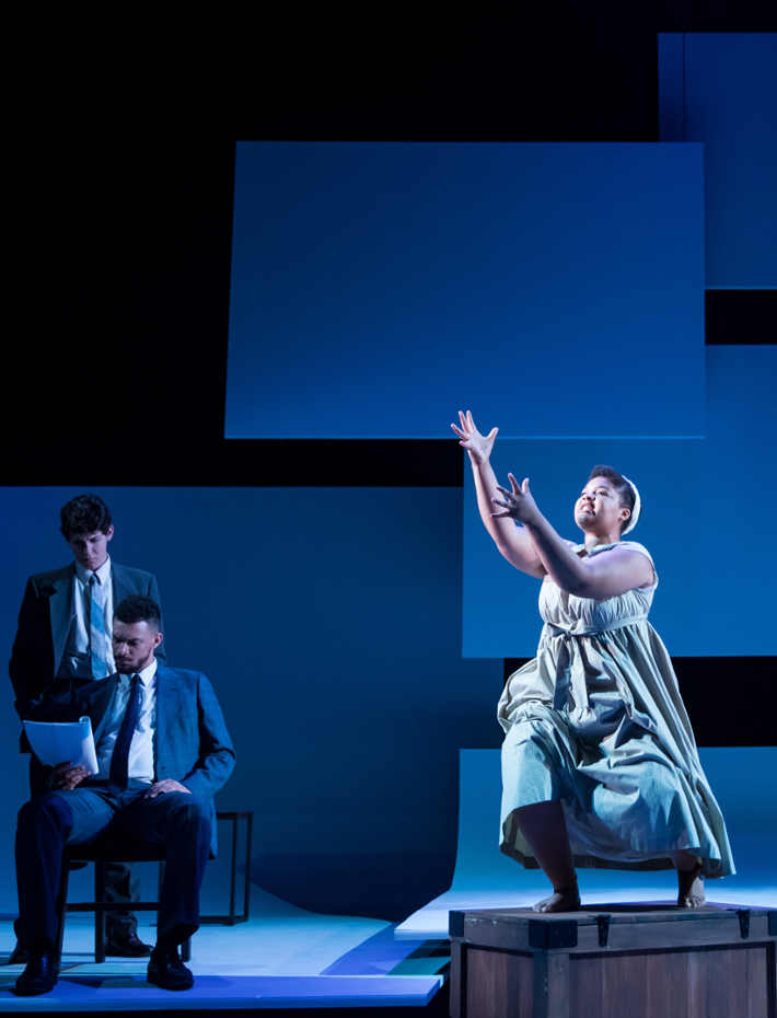 Student actor emotes on stage with two calm actors to her left